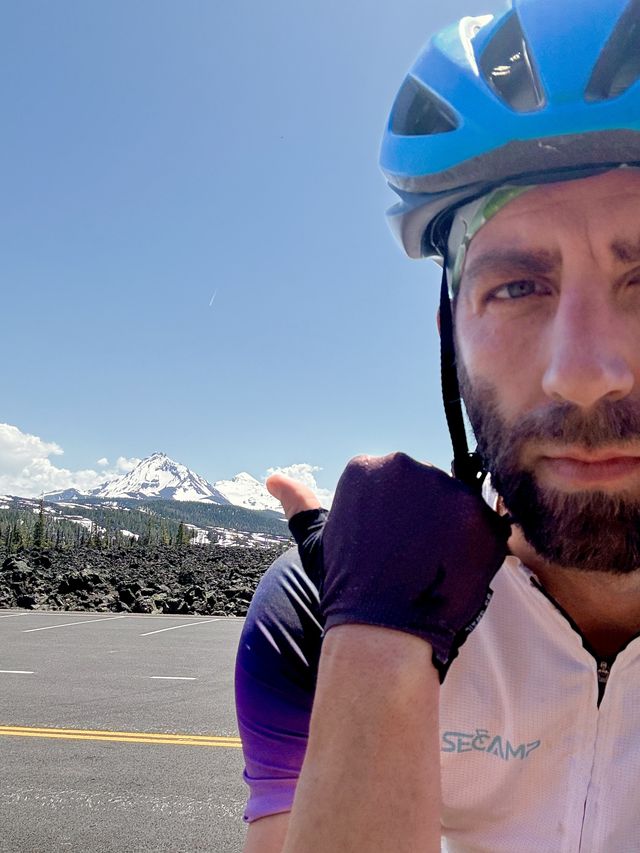 A dork in a bike helmet with the Three Sisters behind him