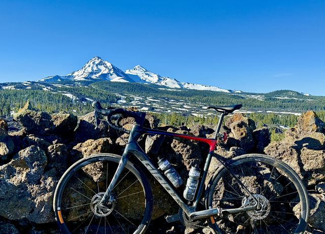 Paul's black Giant Defy road bike against a lava wall with the Three Sisters behind it