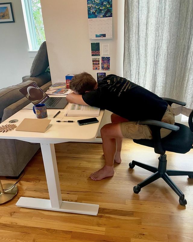 Paul laying his head on his desk with his computer open and study materials all around.