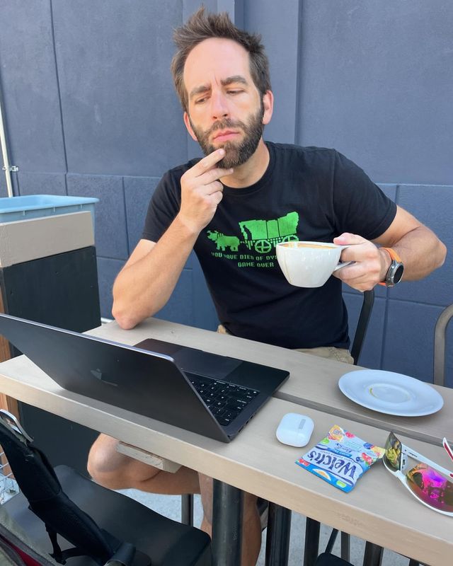 Paul outside on a bench looking at his computer with a goofy contemplative look.